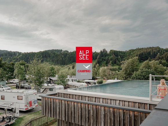 Blick über den Alpsee-Campingplatz mit Pool und Bergen im Hintergrund, vorne das Logo von Alpsee Camping